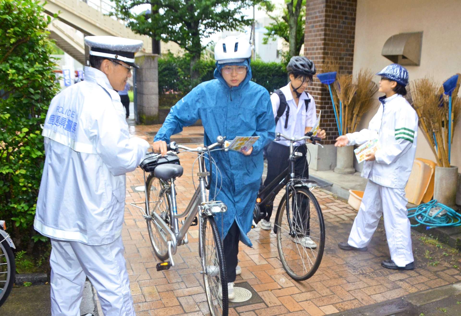 自転車乗車時のヘルメット着用を呼びかけるチラシを手渡す警察官＝１４日午前８時前、鹿児島市の鶴丸高校