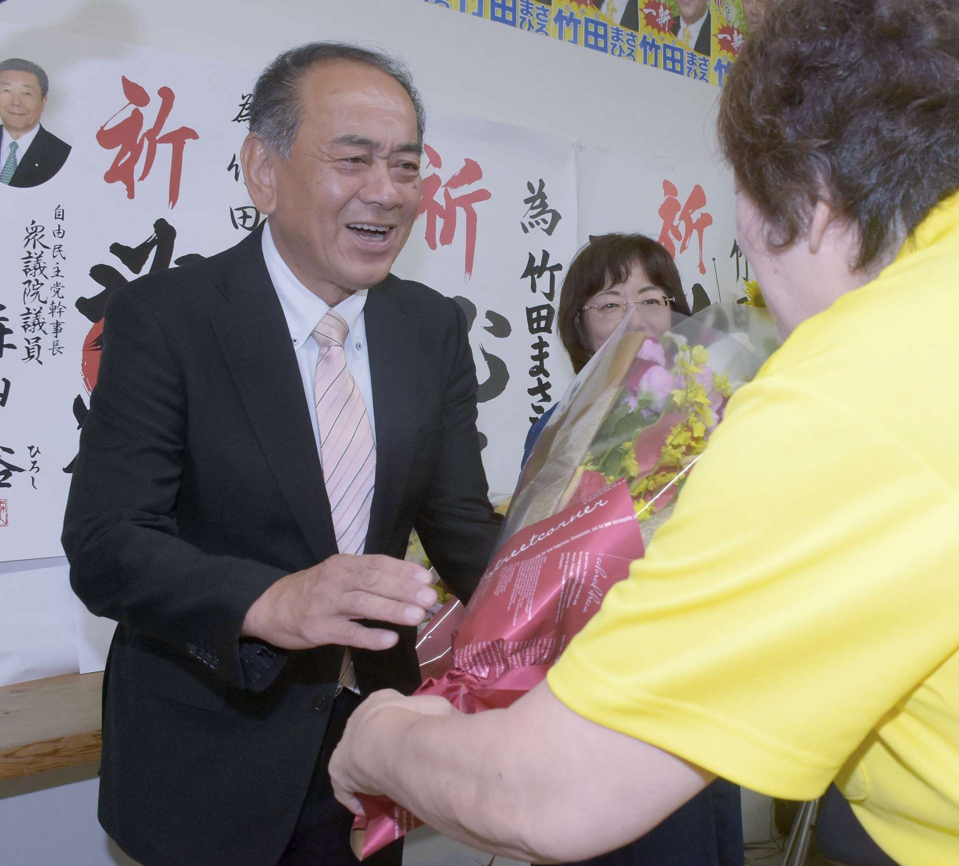 支援者から花束を手渡される竹田正博さん（左）＝２０日午後１０時４５分、曽於市末吉町二之方
