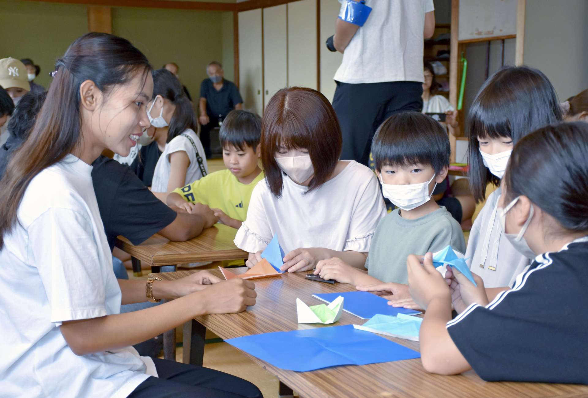 一緒に折り紙で遊ぶ留学生（左）と子どもたち＝いちき串木野市の大原交流センター
