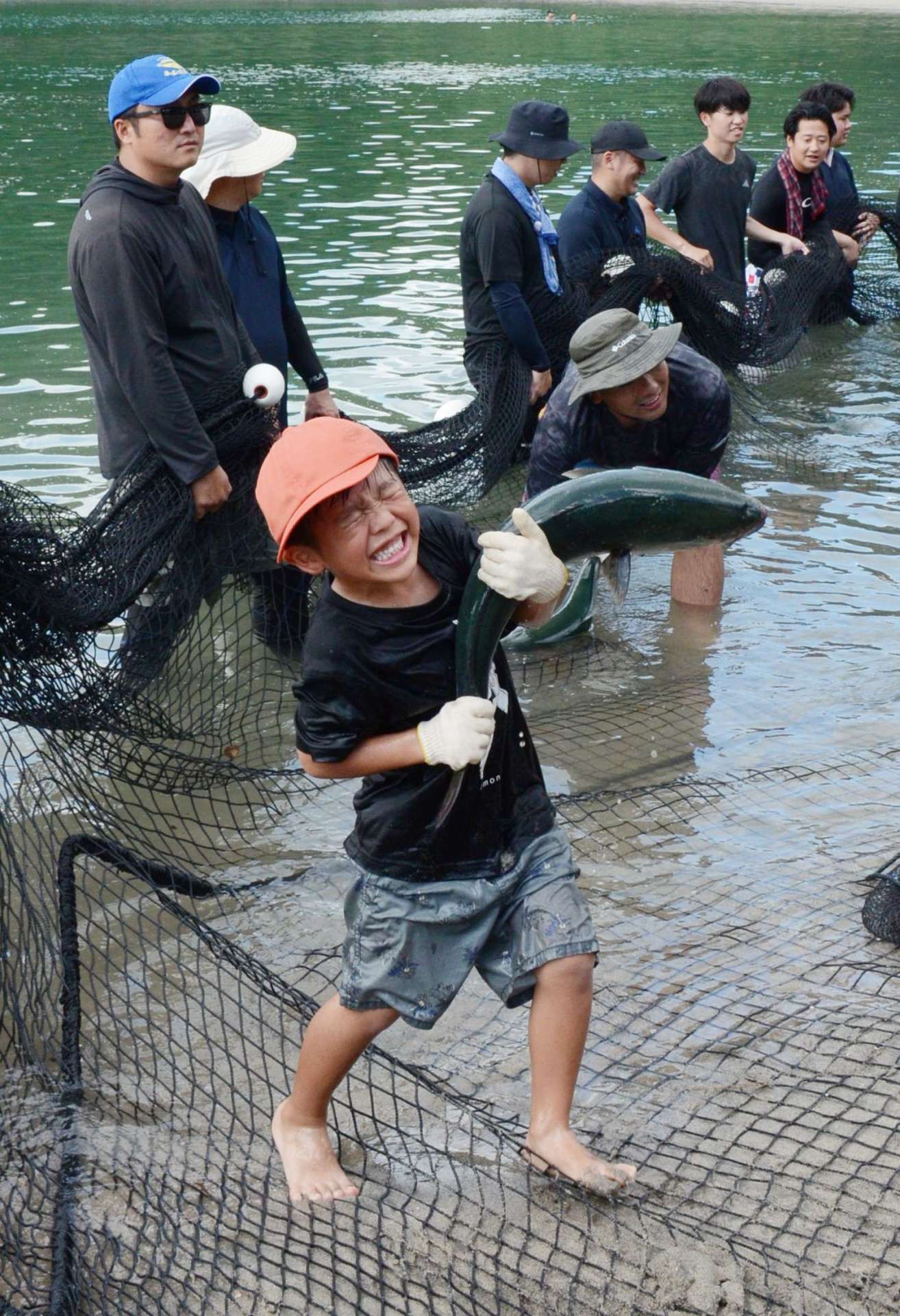 勢いよくはねるブリと格闘する子どもたち＝長島町のあずま海水浴場
