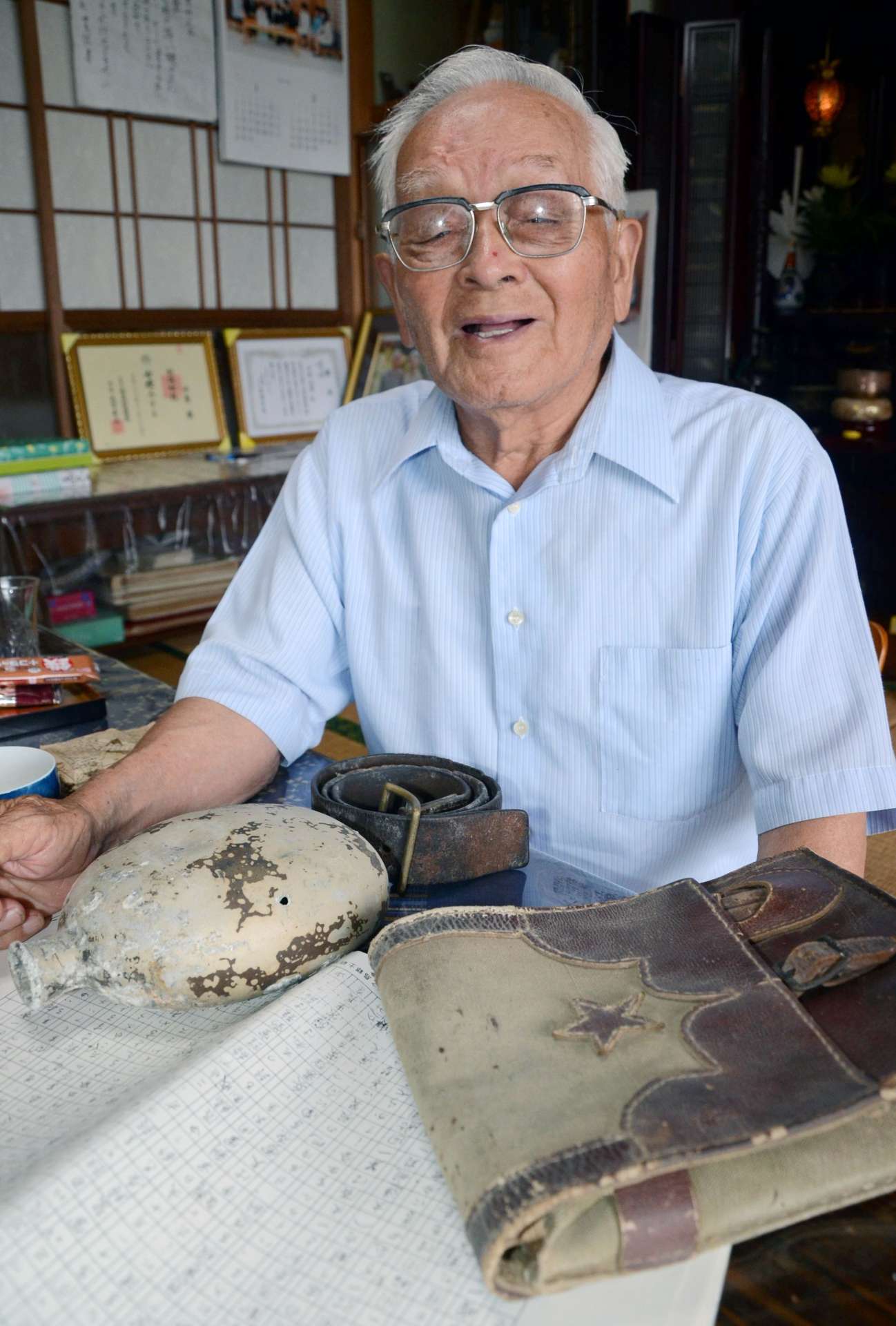 当時のかばんや水筒を前に「死ぬまで悲劇を語り継ぎたい」と話す中原安時さん＝天城町平土野