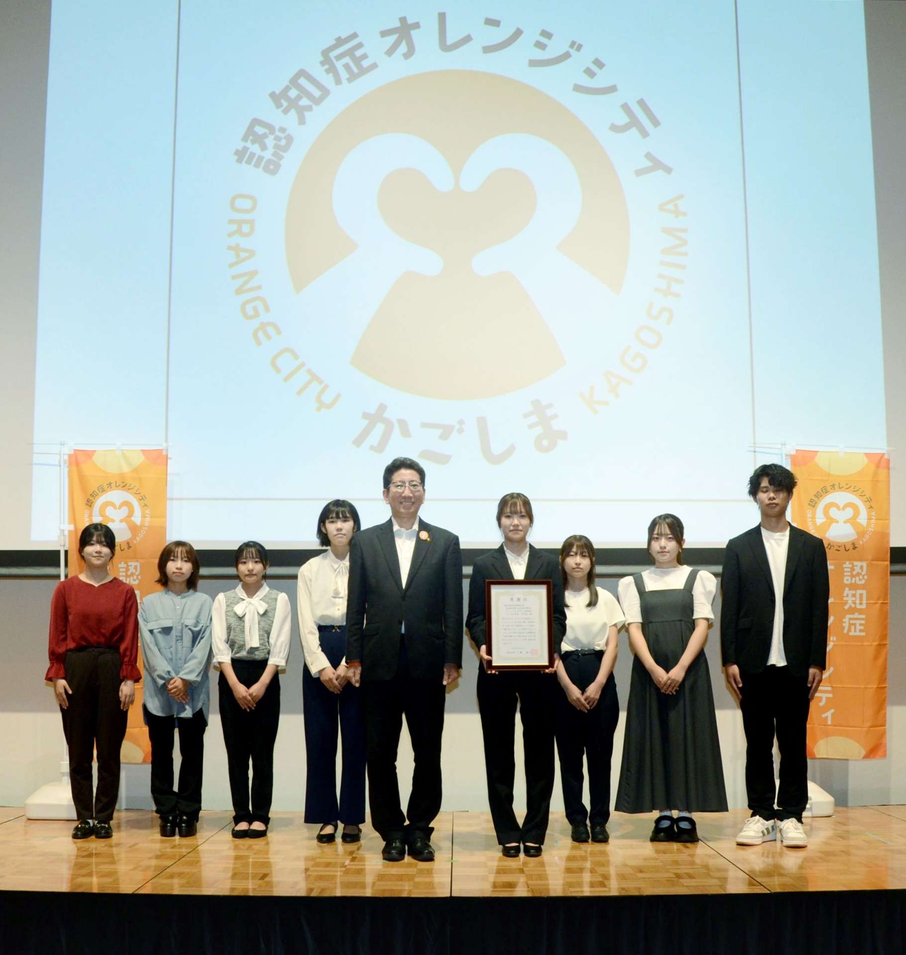下鶴隆央市長（中央）を囲む、「認知症オレンジシティかごしま」のロゴマークを作成した鹿児島県立短大の学生＝３日、鹿児島市のセンテラス天文館