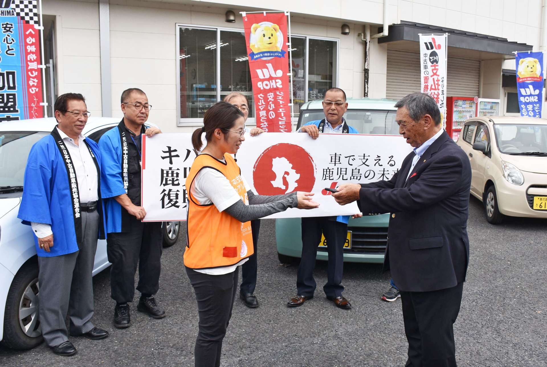 寄贈車両の前でキーを手渡すＪＵ鹿児島の新園康男理事長（右）＝１２日、姶良市加治木