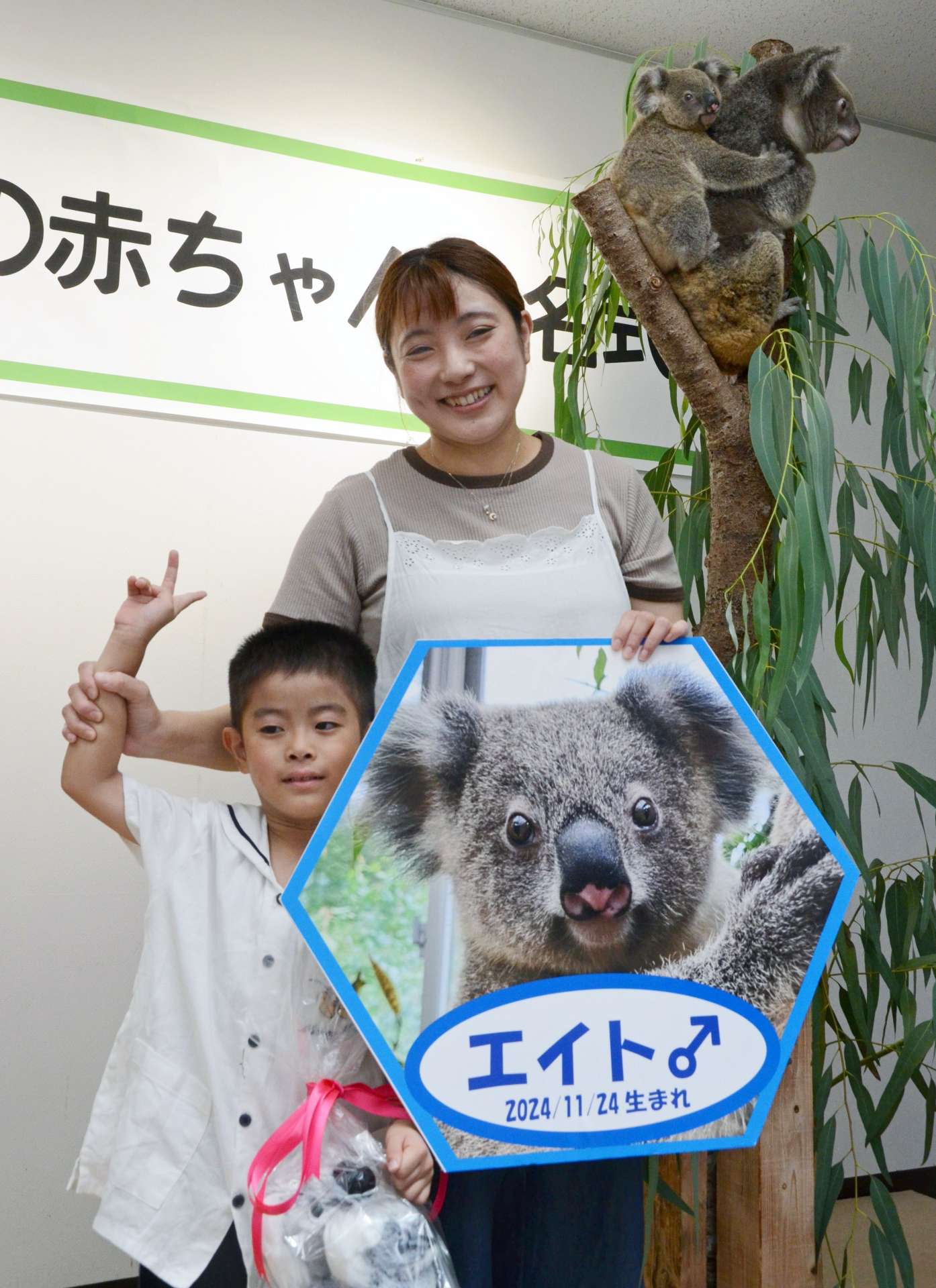 母カナエの背中でエイトが見守る中、記念撮影する名付け親代表のの有川美咲さんと長男英杜さん＝鹿児島市の平川動物公園