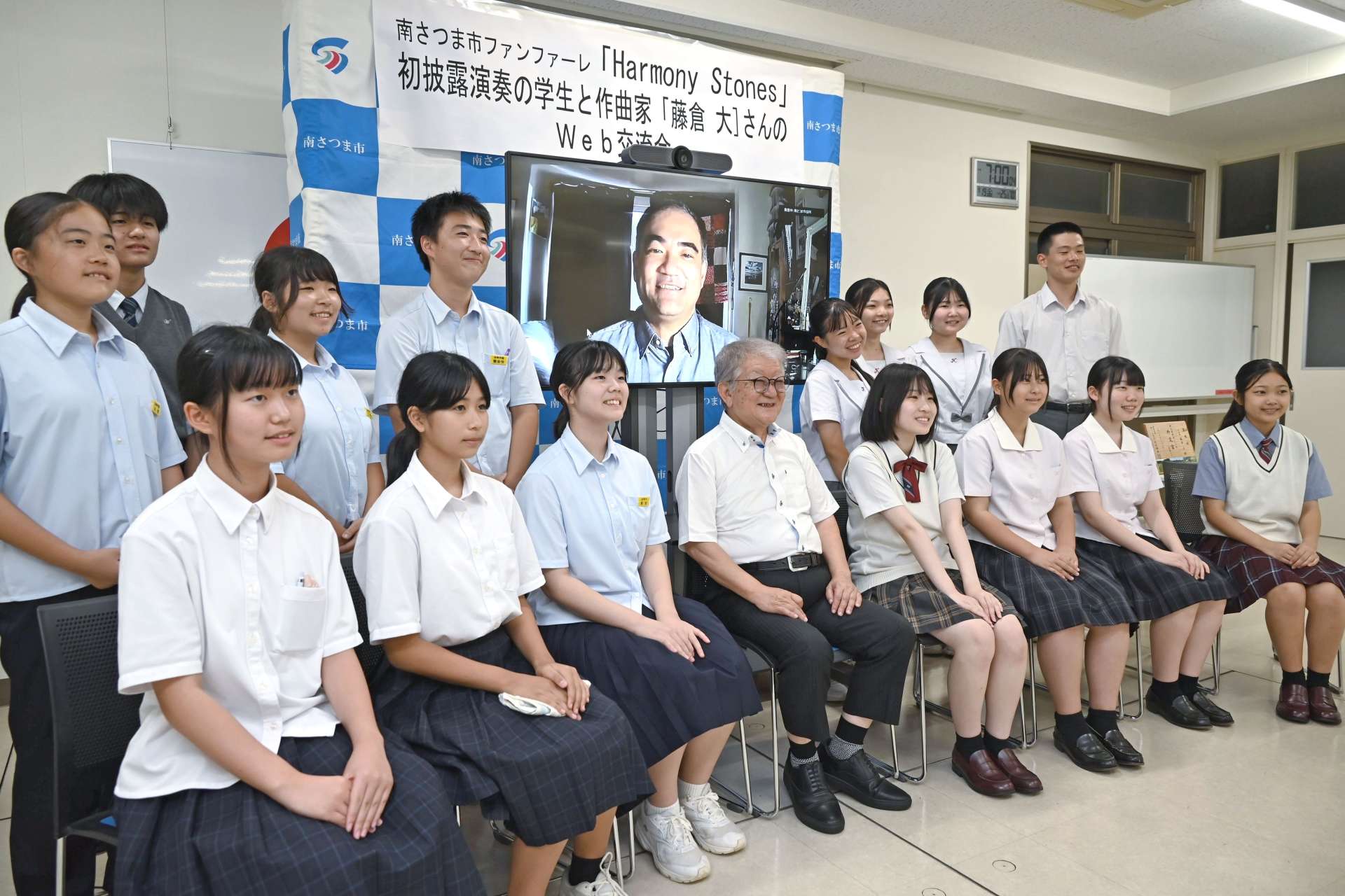 画面に写った藤倉大さんと記念撮影する中高生ら＝１９日、南さつま市役所