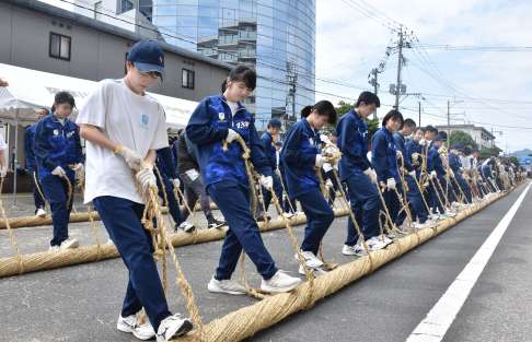 〈長っ…３６５メートル〉繰り返し縄を転がして綱を作る高校生ら＝２２日、薩摩川内市の県道京泊大小路線