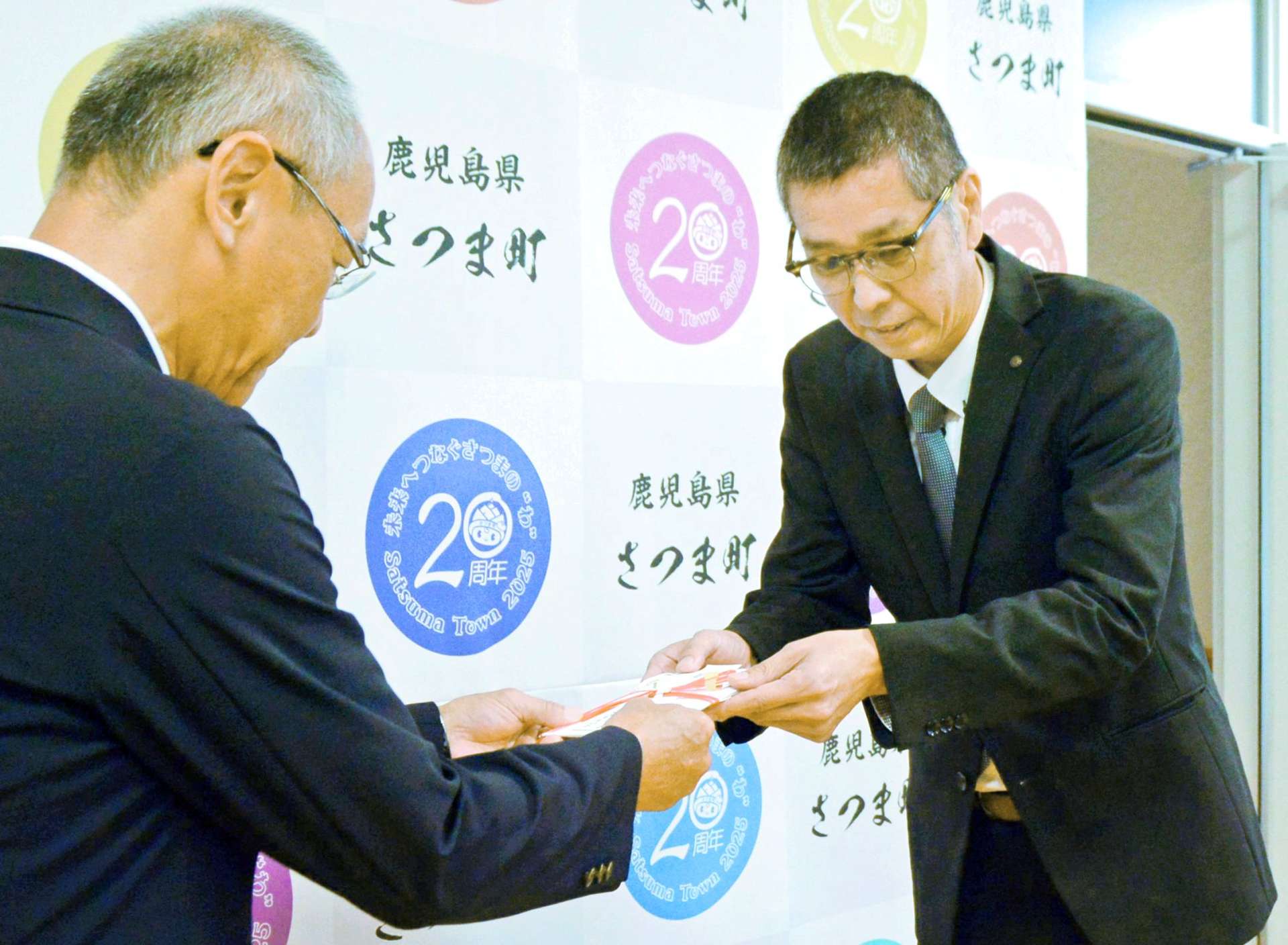 さつま町スポーツ協会に協賛金を寄付する九州郵便局長協会薩摩部会の米森聖司部会長（右）＝さつま町役場