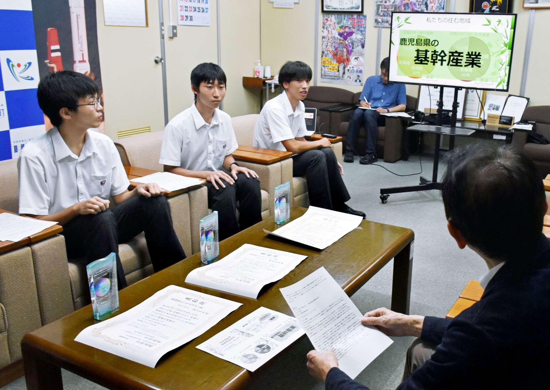 永野和行町長に受賞時のプレゼンを紹介する楠隼高校の生徒３人＝肝付町役場