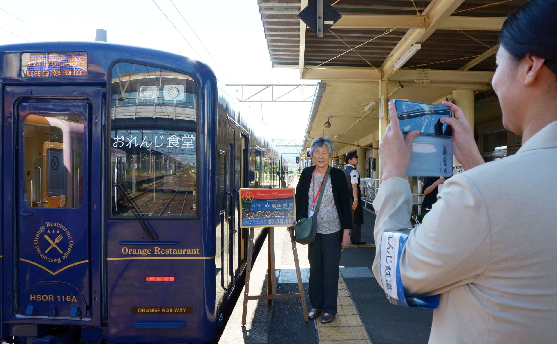 観光列車「おれんじ食堂」と記念撮影するクルーズ客＝６日、出水市の肥薩おれんじ鉄道出水駅
