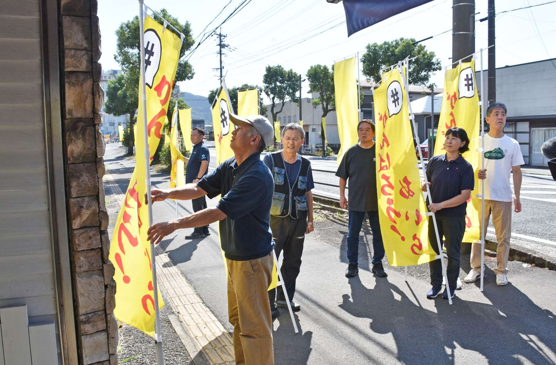 国道１０号沿いに黄色い旗を立てる網掛橋復興臨時通り会のメンバー＝７日、姶良市加治木