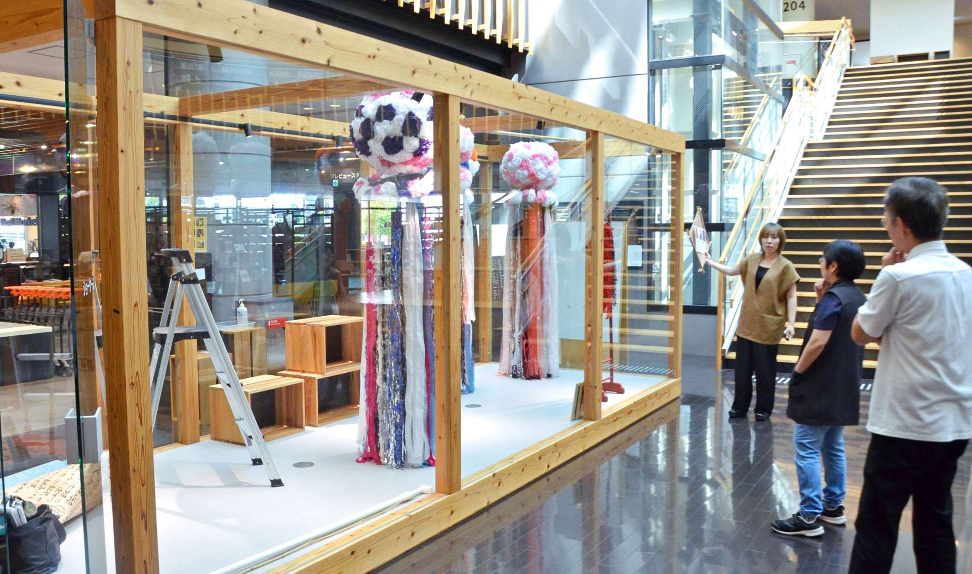 都城市立図書館関係者と相談しながら「千日夜市」の告知スペースの展示に当たる鎌田美里さん（写真右から３人目）＝同市中町
