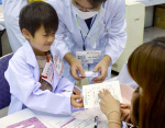 仕事体験で調剤した薬を説明する小学生（左）＝１２日、鹿児島市の西原商会アリーナ