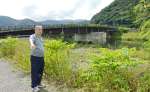 奄美豪雨で氾濫した住用川沿いに立つ満田英和さん＝２０日、奄美市住用町西仲間