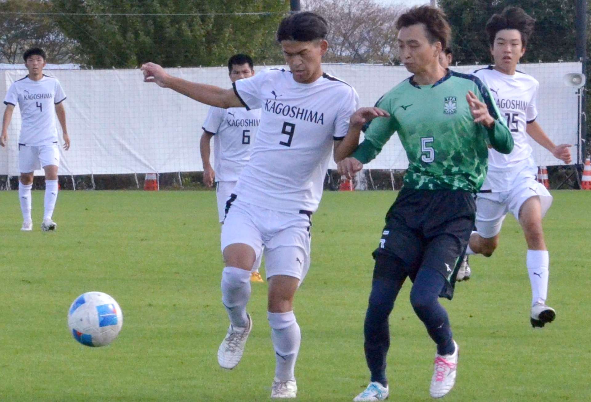 前半、球際で競り合うサッカー鹿児島チームのＦＷ海老原蓮＝２７日、滋賀県守山市の野洲川歴史公園サッカー場