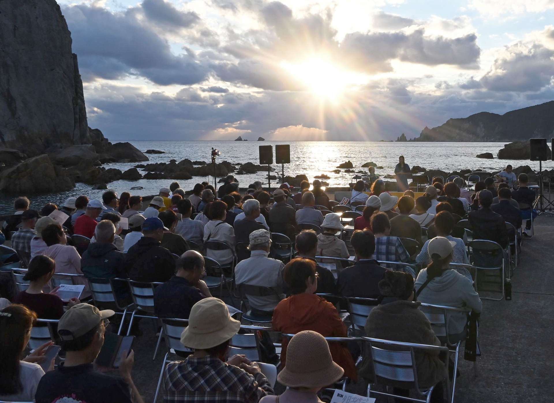 野間岬と立神の間に沈む夕日を眺めながらコンサートを楽しむ来場者＝南さつま市笠沙の後浜