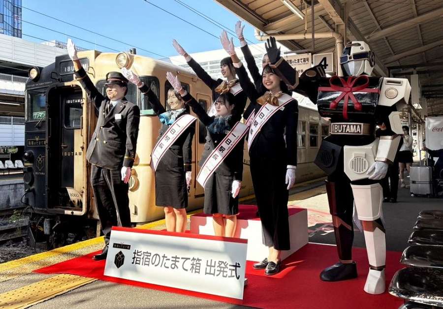 出発式で合図を送る「いぶたマン」やＨＫＴ４８のメンバー＝３日、鹿児島市のＪＲ鹿児島中央駅