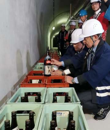 坑道貯蔵を示す専用ラベルを焼酎に貼る蔵元の代表ら＝５日、鹿児島市の桜島有村観測坑道