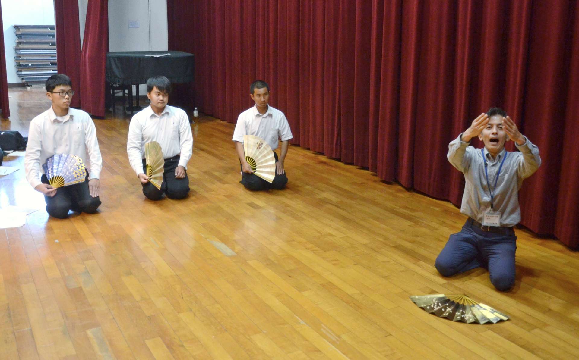 １００周年記念式典に向け、狂言師の山下守之さん（右）から指導を受ける生徒３人＝日置市の吹上高校