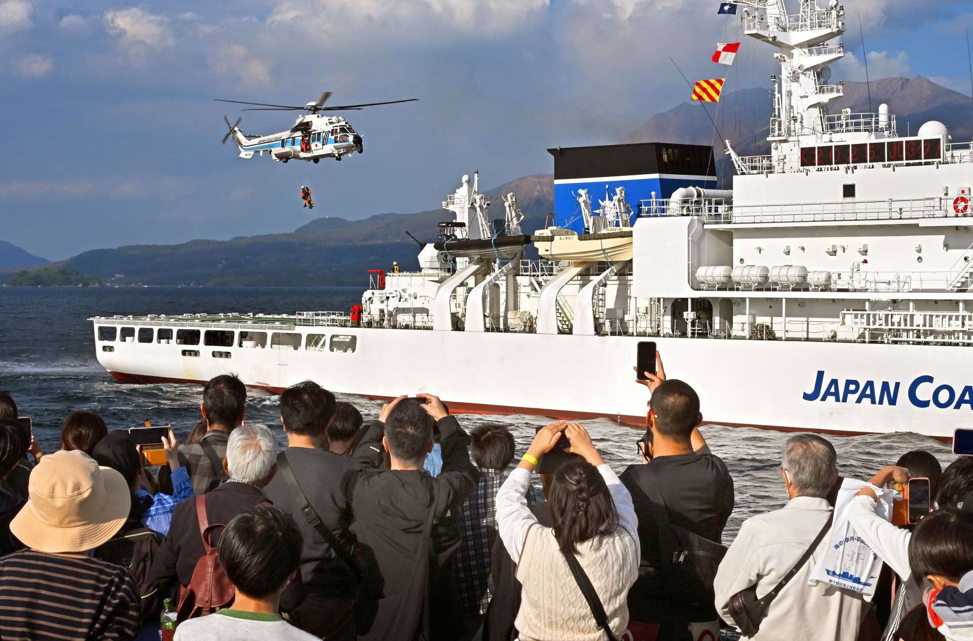 ヘリコプターを使ったつり上げ救助訓練に見入るＪＣＧクルーズの参加者＝鹿児島湾