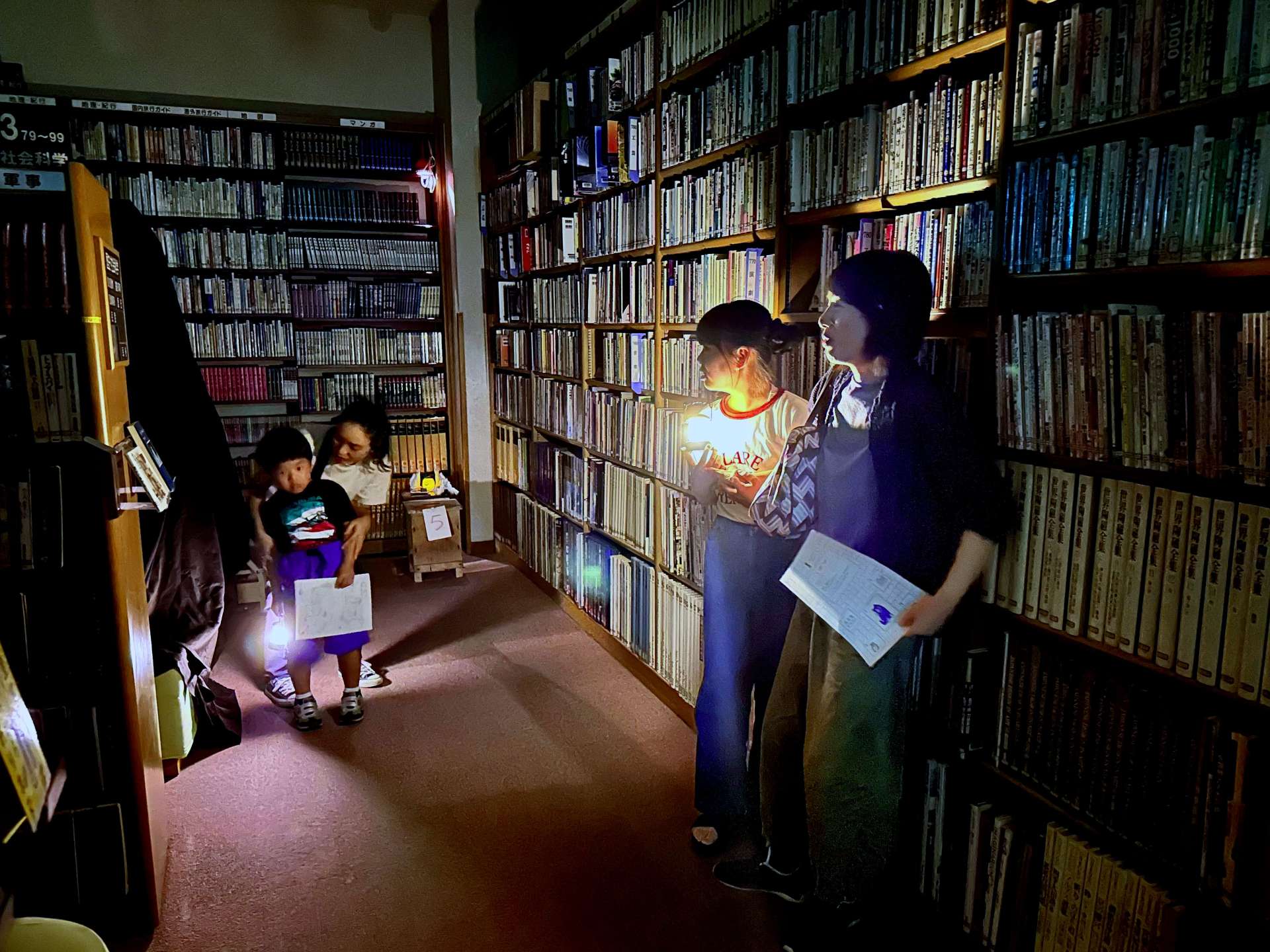 明かりを頼りに真っ暗な図書室を探検する参加者＝南九州市の知覧図書館