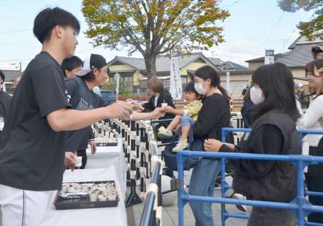 ロッテ選手（左）から炭火焼きを受け取るファン＝都城市妻ケ丘町