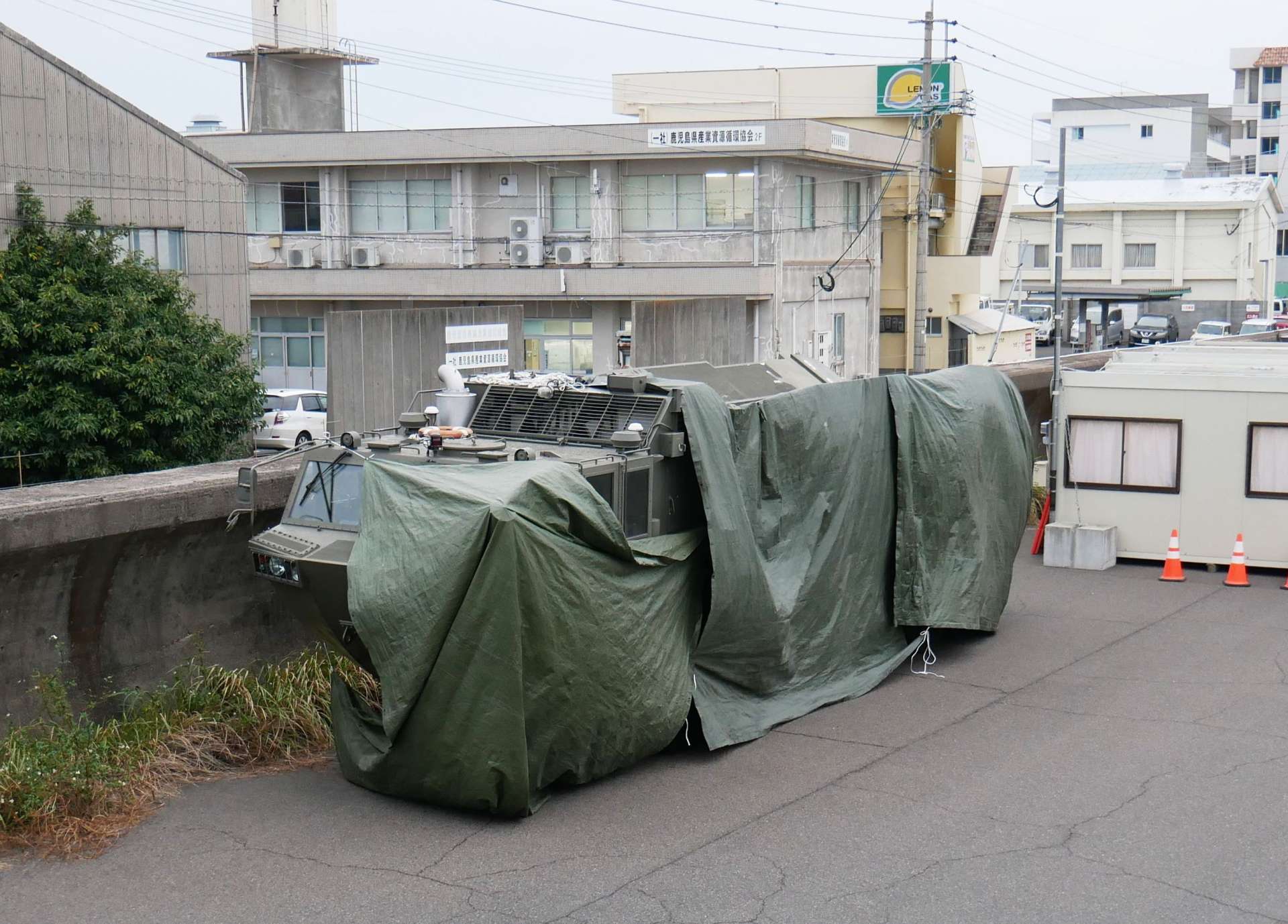 〈引いたアングルの写真を見る〉幕をかぶり、ひっそりと応援を待つ水陸両用車＝１２日、鹿児島市錦江町