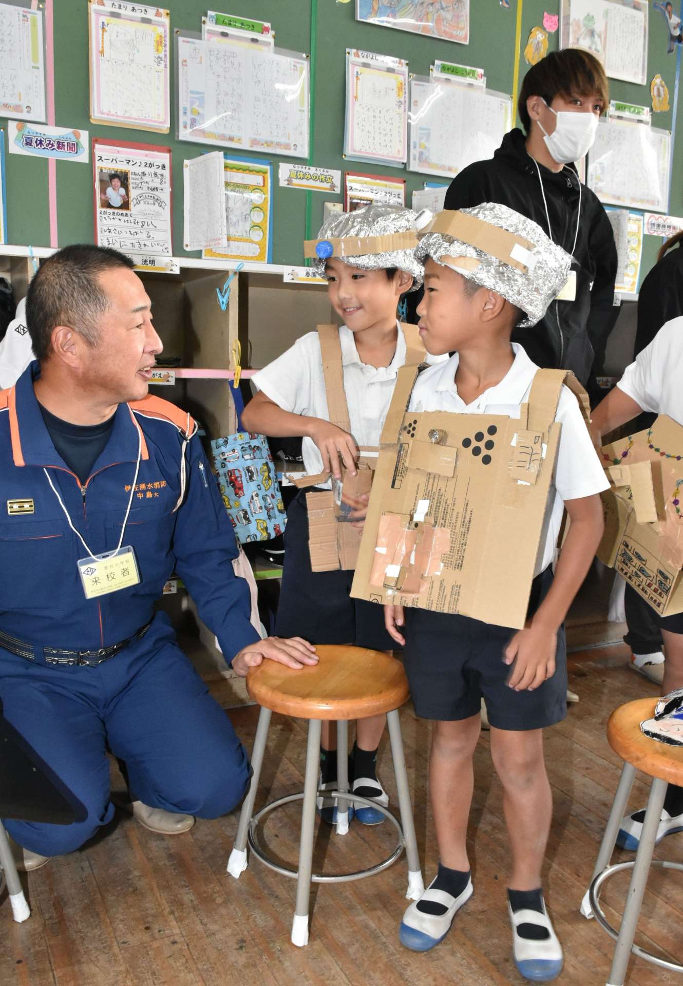 見学した菱刈分遣所の中島大陽所長（左）に自作の消防服、ヘルメットを見せる児童ら＝伊佐市の菱刈小学校