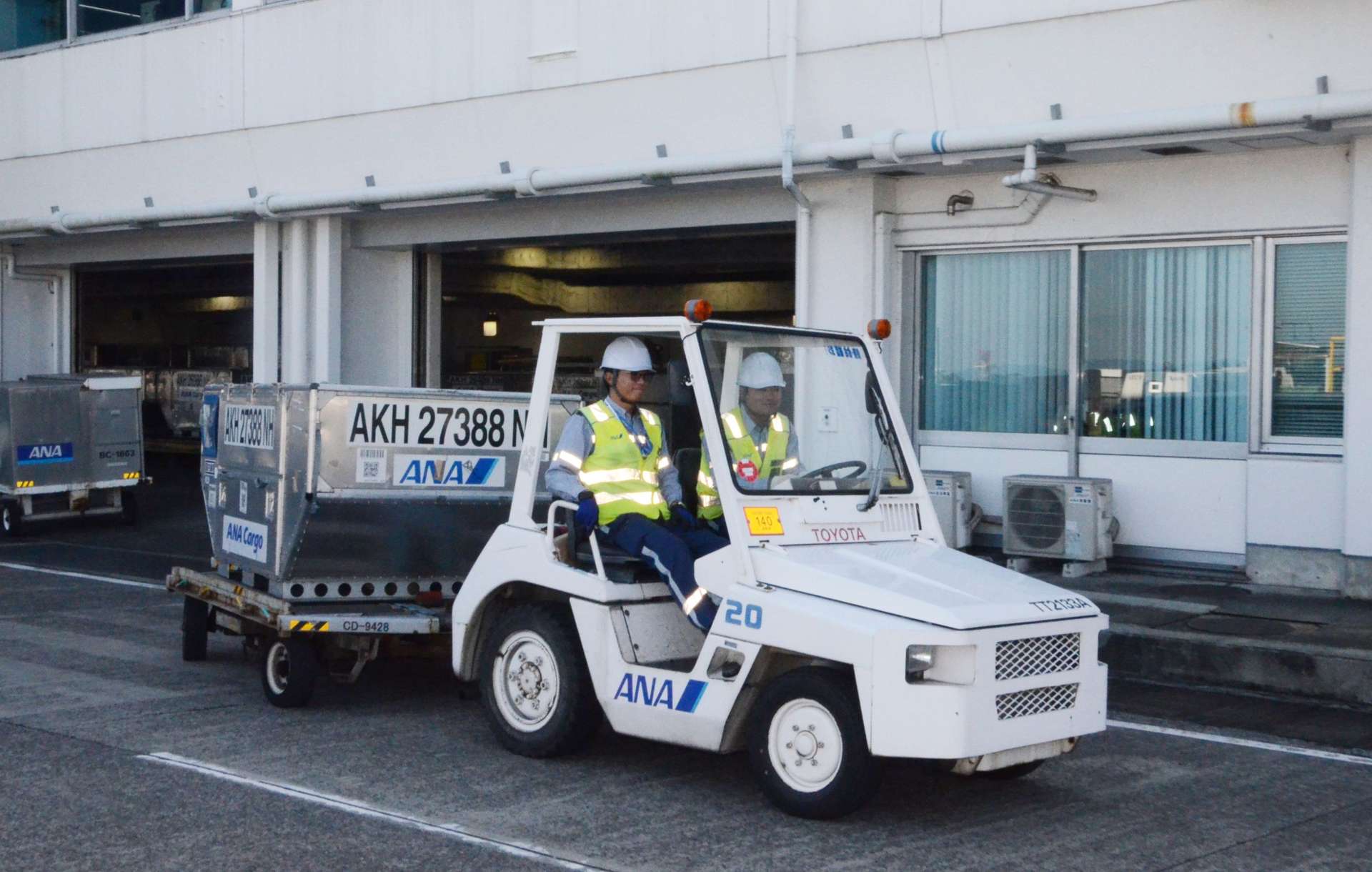 コンテナをけん引する特殊車両に乗車する宮原さん（左）と青山さん＝１４日、霧島市の鹿児島空港