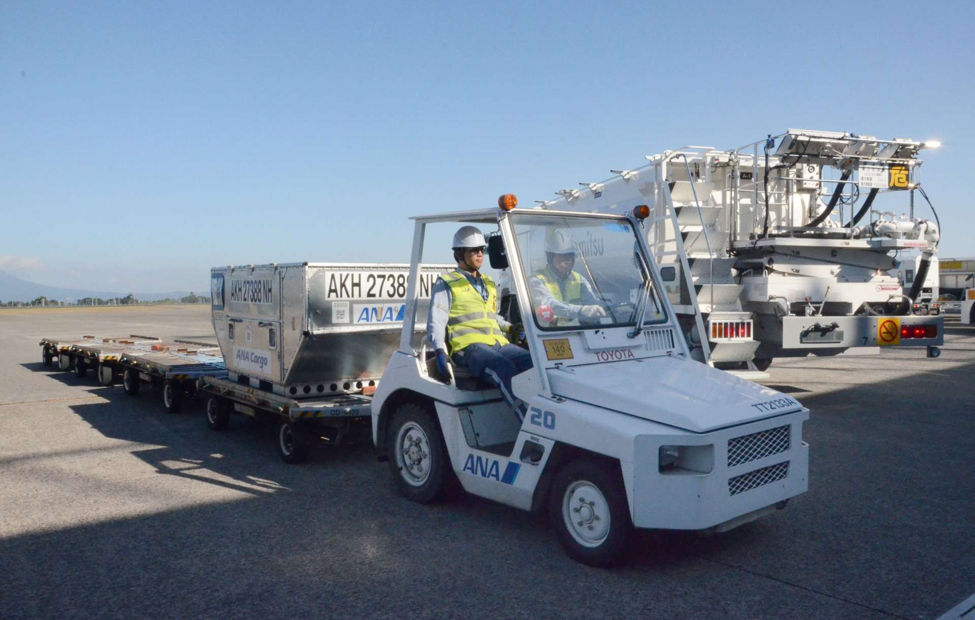 コンテナをけん引する特殊車両に乗車する宮原さん（左）と青山さん＝１４日、霧島市の鹿児島空港