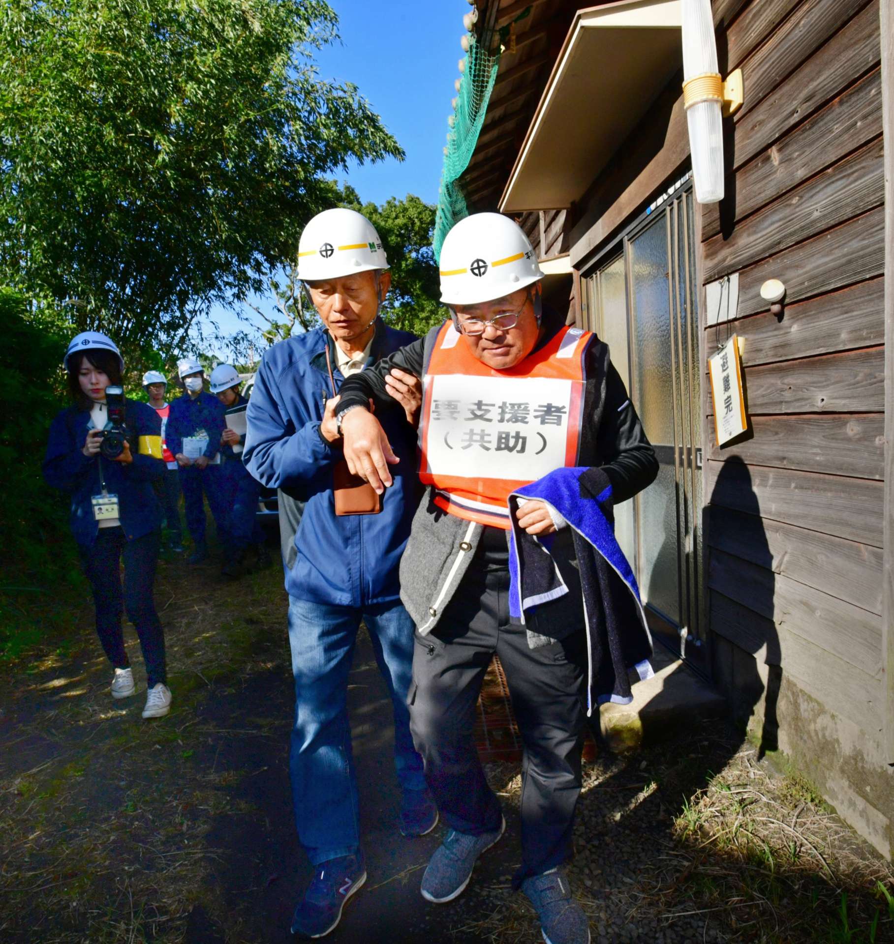 避難のため、付き添われて車両まで移動する住民＝１５日午前９時２５分、鹿児島市桜島西道町