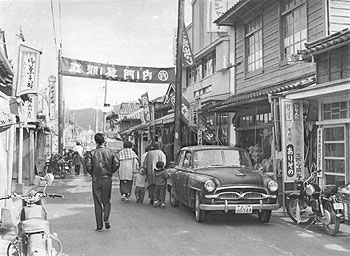 昭和34年、旧川辺町の商店街。「この数年来めきめき充実し、およそ二キロにおよぶメイン・ストリートが形成されている。農村で繁華街が二キロも続いているところは珍しく、バックには豊かな農村経済の力のあることが想像される」