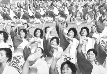 昭和４７年１０月、太陽国体開会式集団演技。手を高くかざし、薩摩女の心意気を踊る婦人たち。紙面では「鹿児島県内の全市町村の婦人が参加した国体の集団演技『よかとこさつま』。離島の５０人は“内地”の2000人に負けなかった。笑みを浮かべ、手を大きくあげる婦人たち。それは太陽の下、厳しい自然の中でたくましく生きる薩摩女の心意気そのものだった」と報じている。