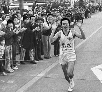 昭和４９年２月１１日、駅伝第２日、日間優勝をとげ、テープを切る出水のアンカー神之門選手。紙面では「第２日の１１日は午前８時、加世田市役所前をスタート、出水市役所前までの１０区間１１７．３キロで行った。前日のリードをさらに広げようという鹿児島、一気に逆転、総合優勝をねらう肝付、郷土入りを飾ろうという出水が激しいトップ争い。結局、出水が４区から首位に立ち、そのままゴールして日間優勝」と報じている。
